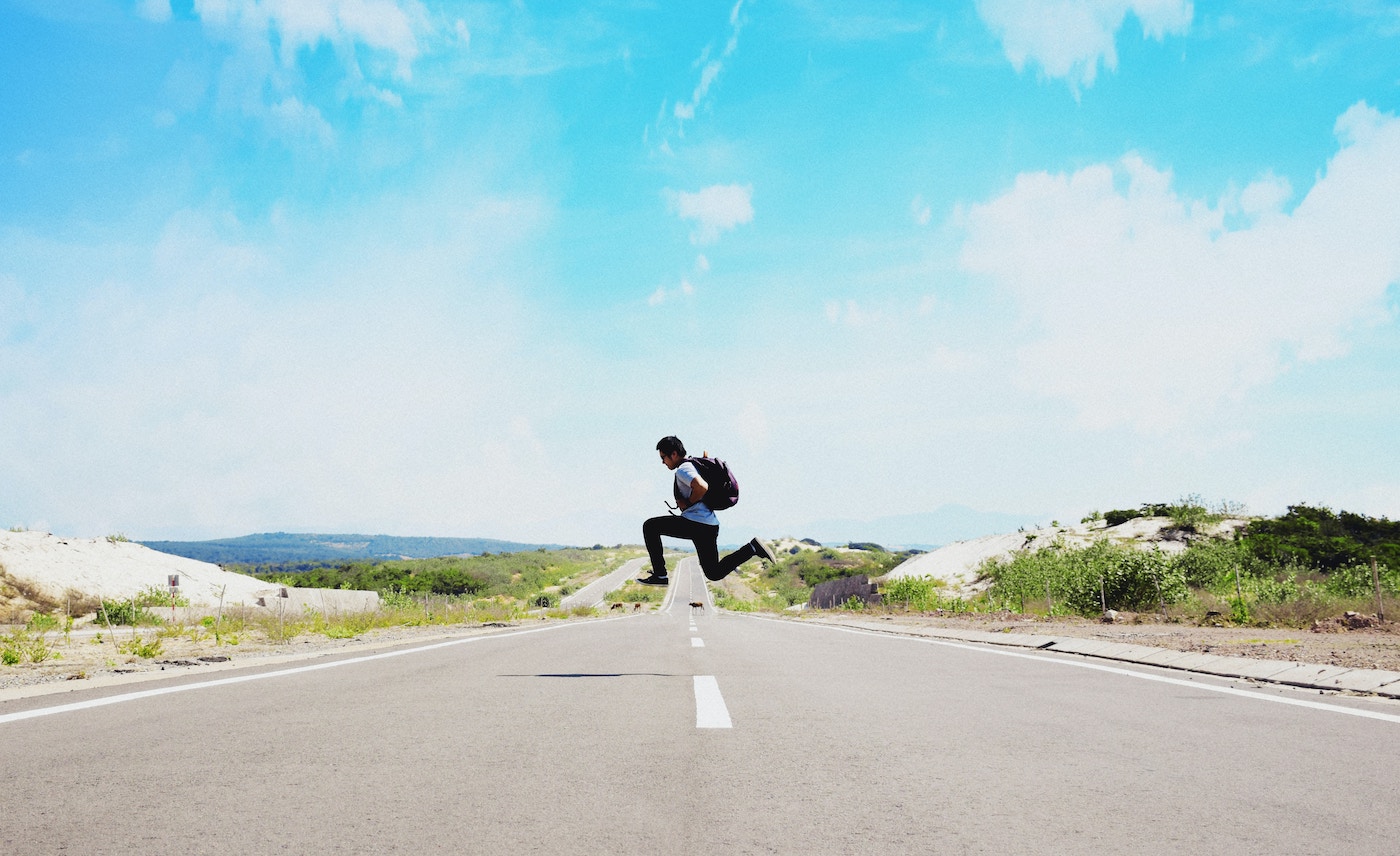 Traveler jumping in the middle of a road